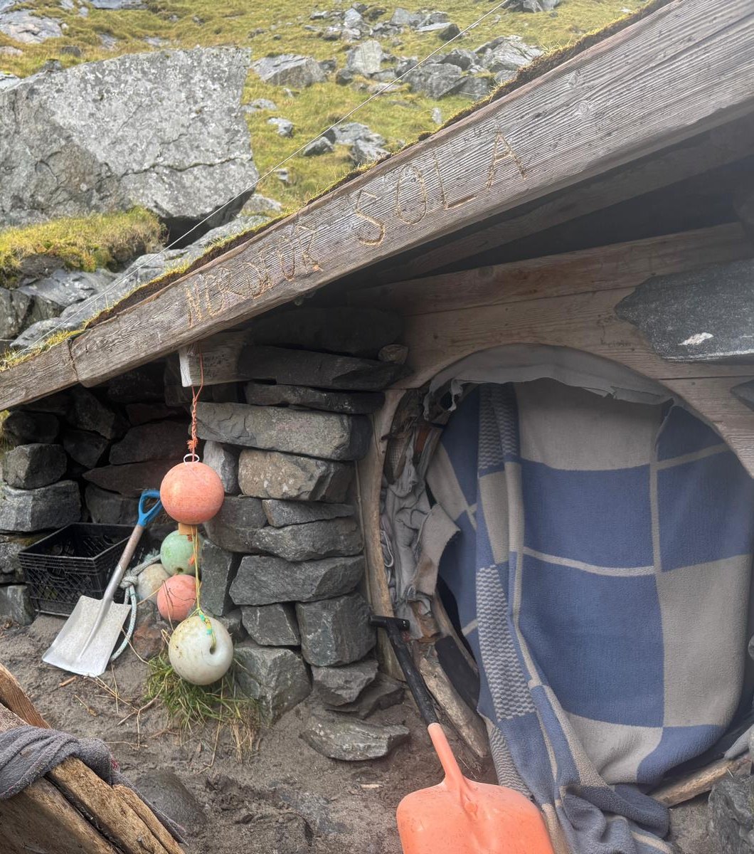 One of the hosts outside the driftwood-and-stone cabin at Kvalvika, with the name carved into the roof beam.