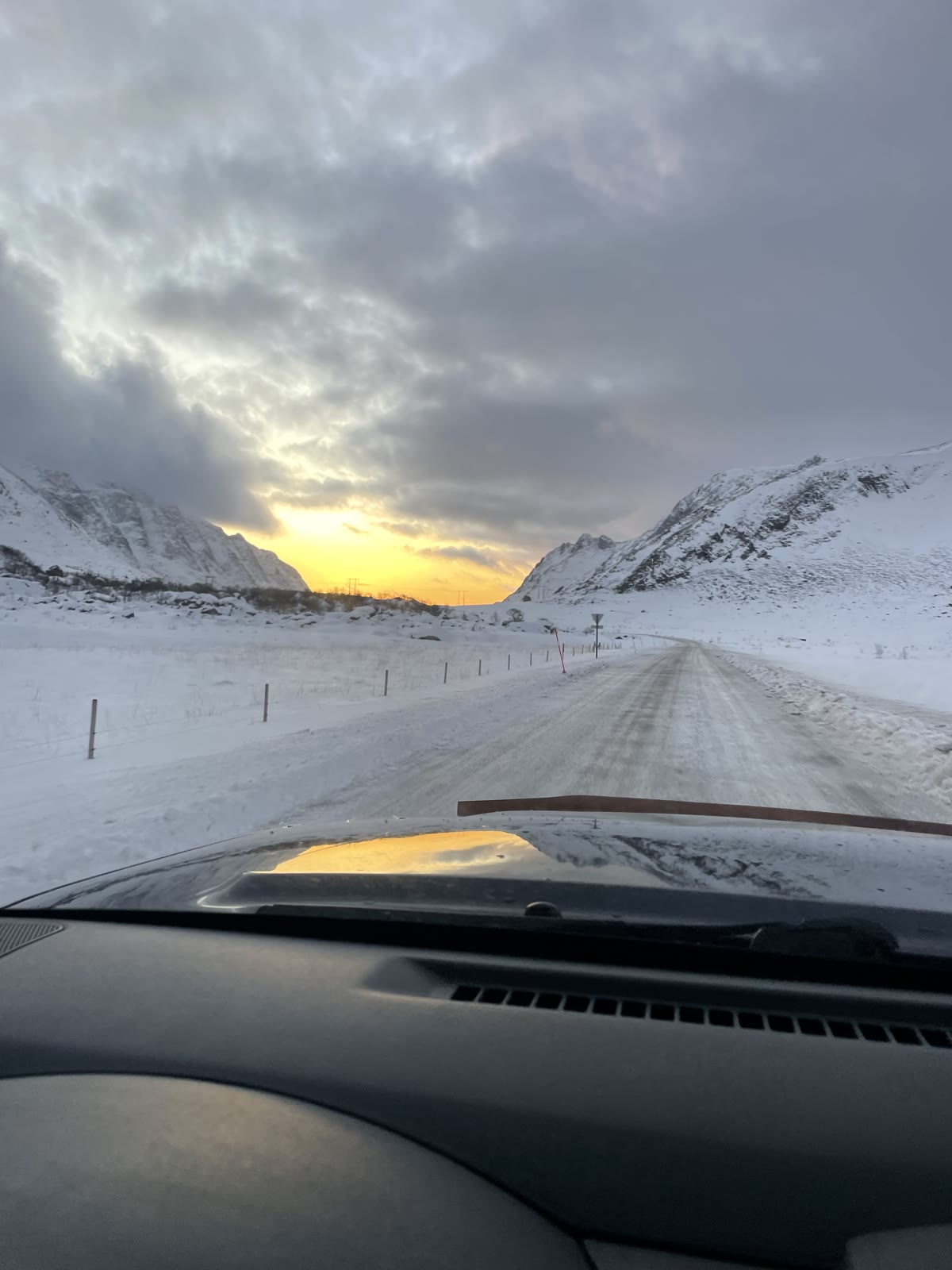 The ploughed road between snowy peaks at winter sunset, seen from the car.