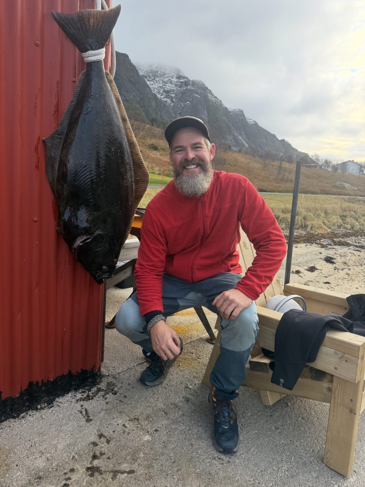 Vegard by the red wall, a large halibut hung up beside him.