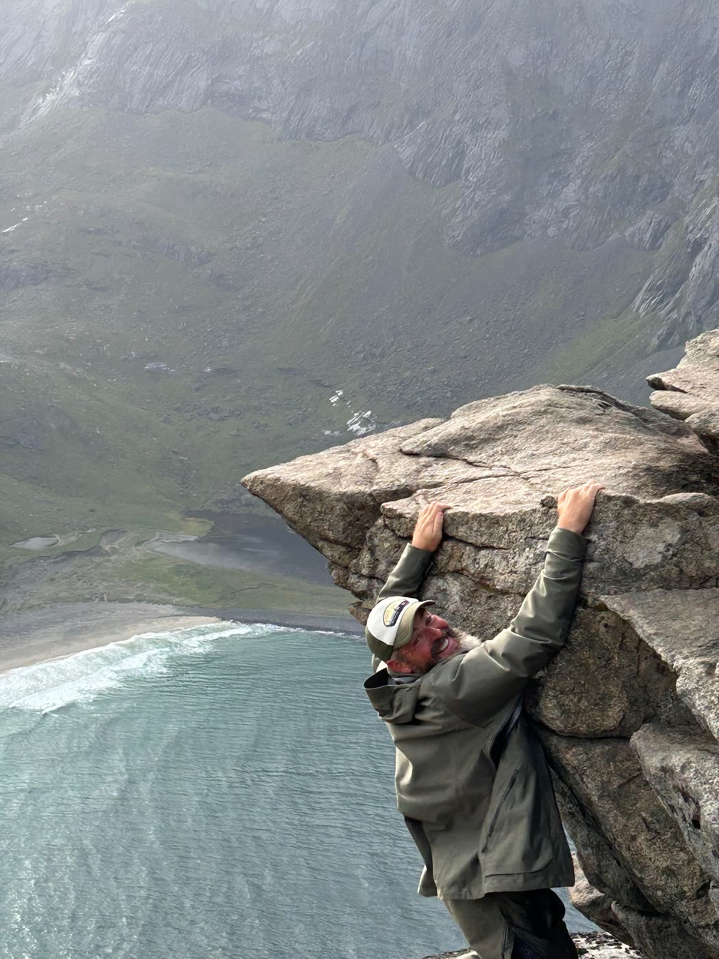 A hiker hanging from the Ryten cliff edge above Kvalvika