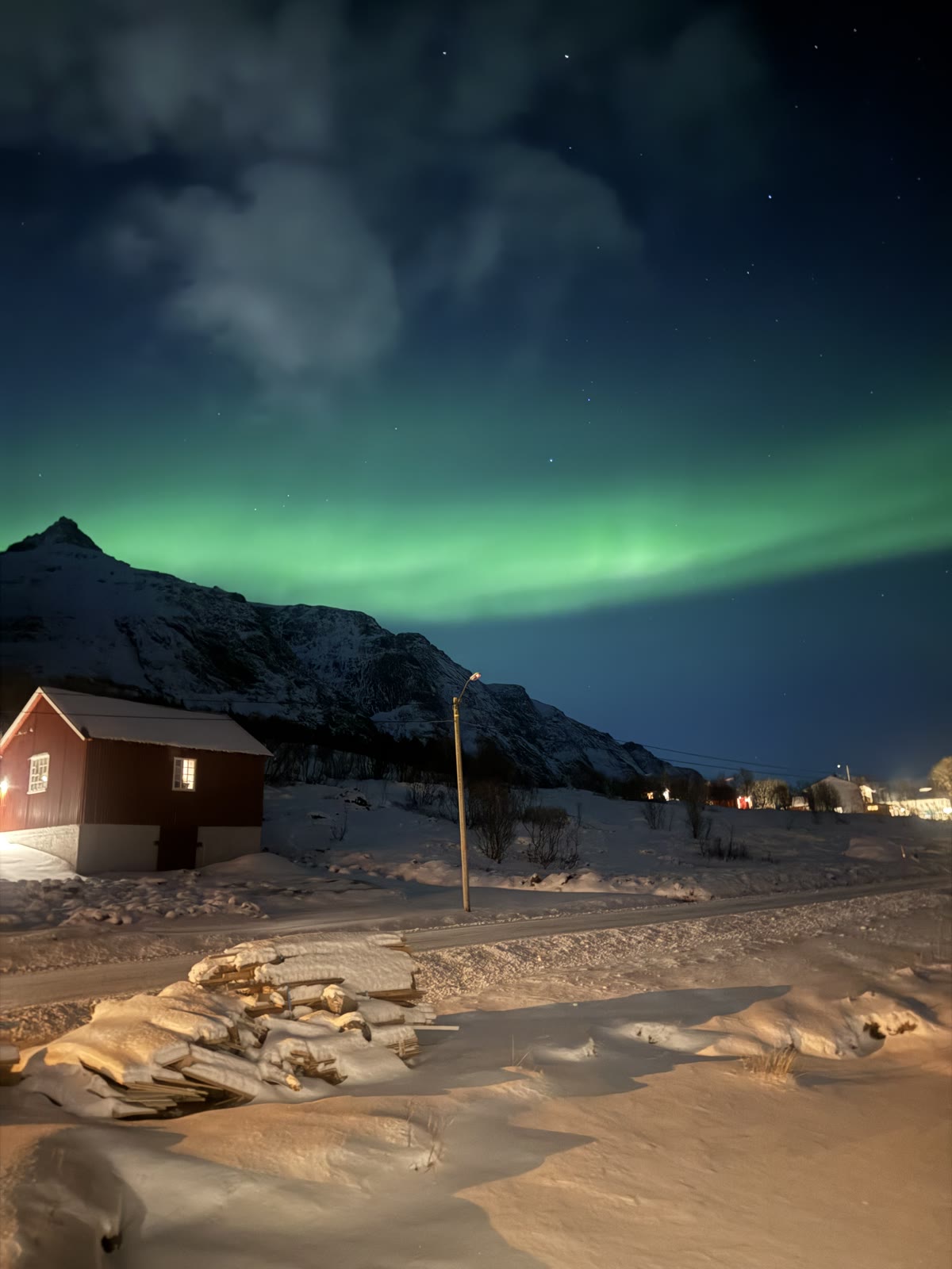 Northern lights over a red cabin and snowy peaks in winter.