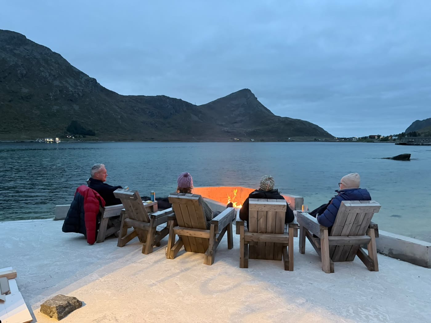 Guests around the fire bowl on the shore at blue hour.