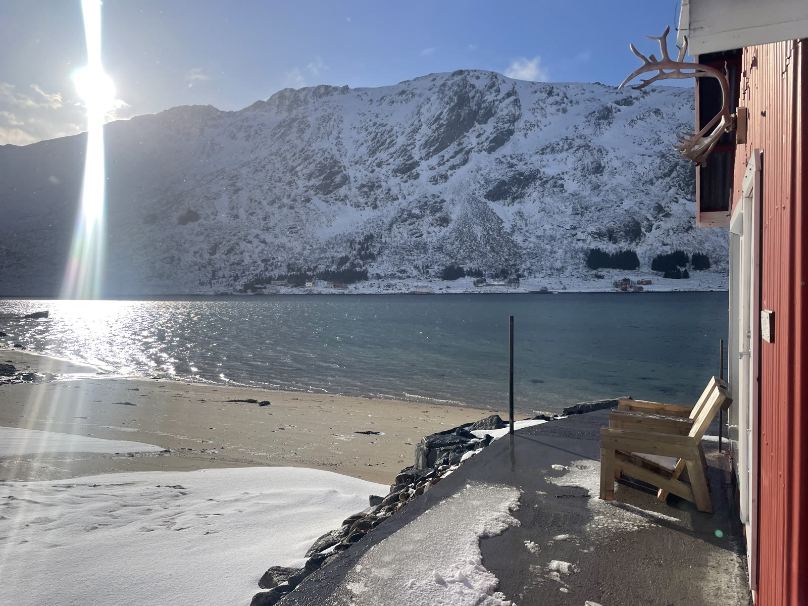 Sunlit snow-capped peaks over an ink-blue spring sea, from the beach by the house.