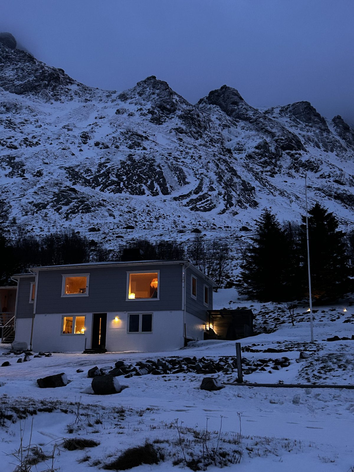 The main house seen from the beach in the winter blue hour, lights on in the windows.